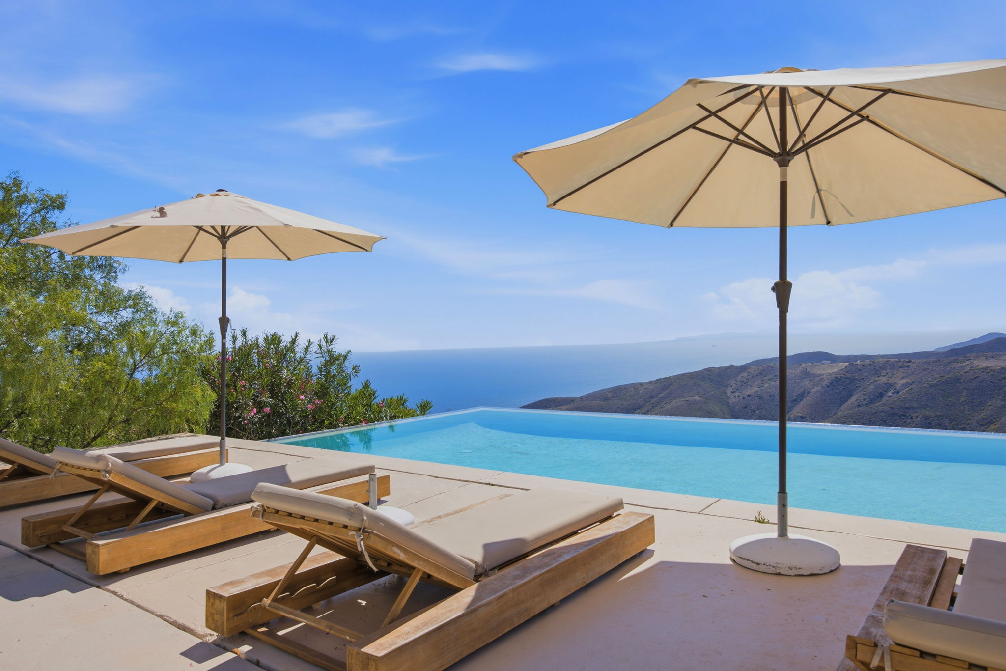 Infinity-edge pool and spa dissolving into the Pacific horizon, teak loungers under umbrellas