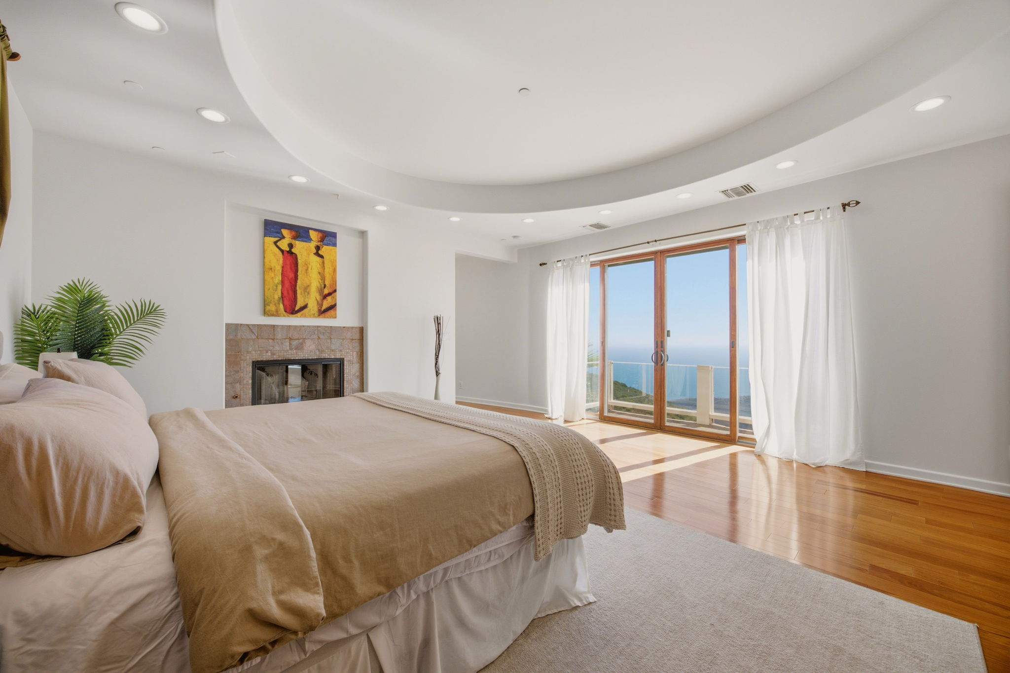 Primary bedroom with curved ceiling cove, fireplace, and French doors opening to an ocean-view balcony