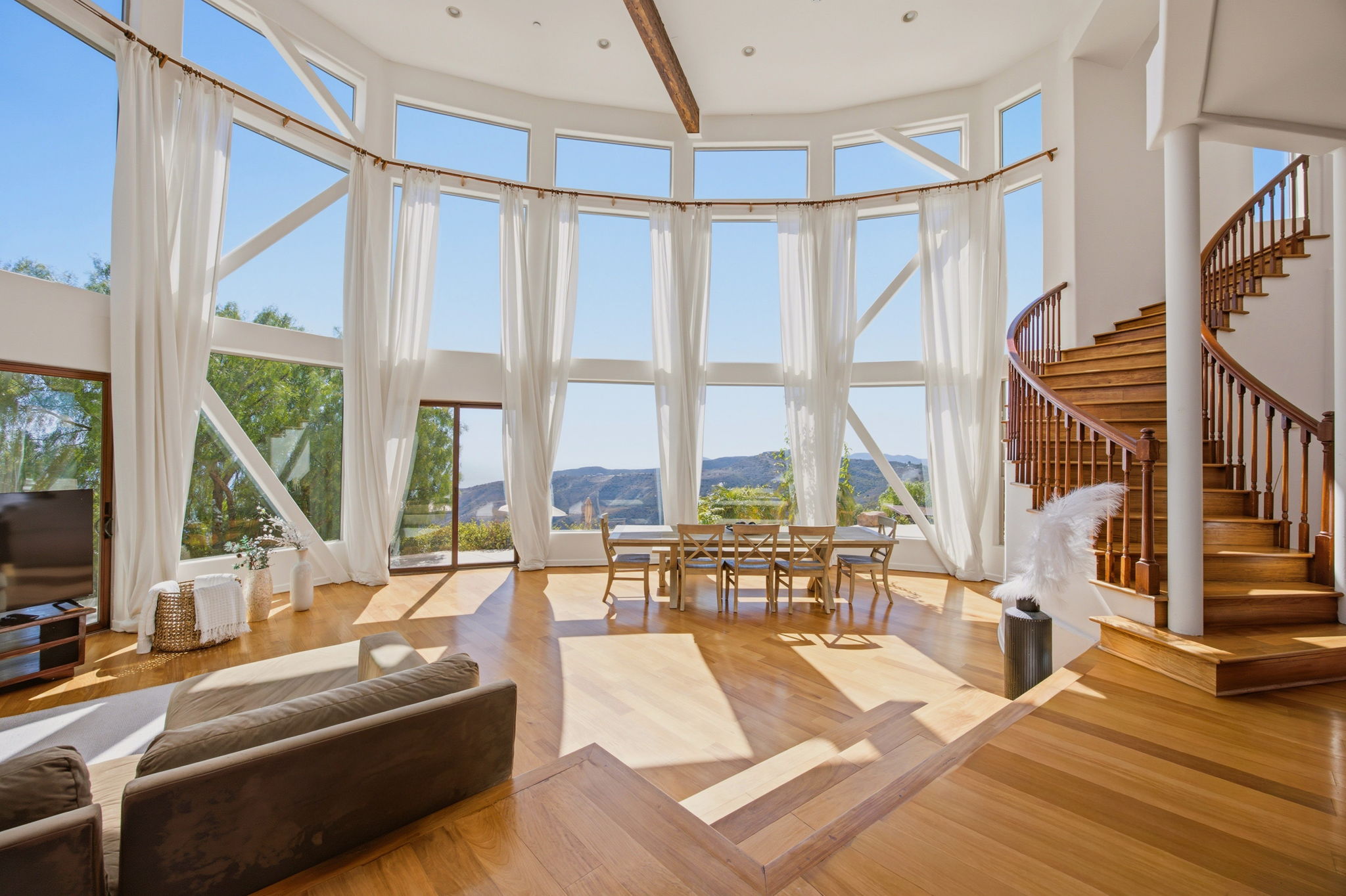 Double-height great room with a curved wall of windows, sheer drapes, and a mahogany spiral staircase