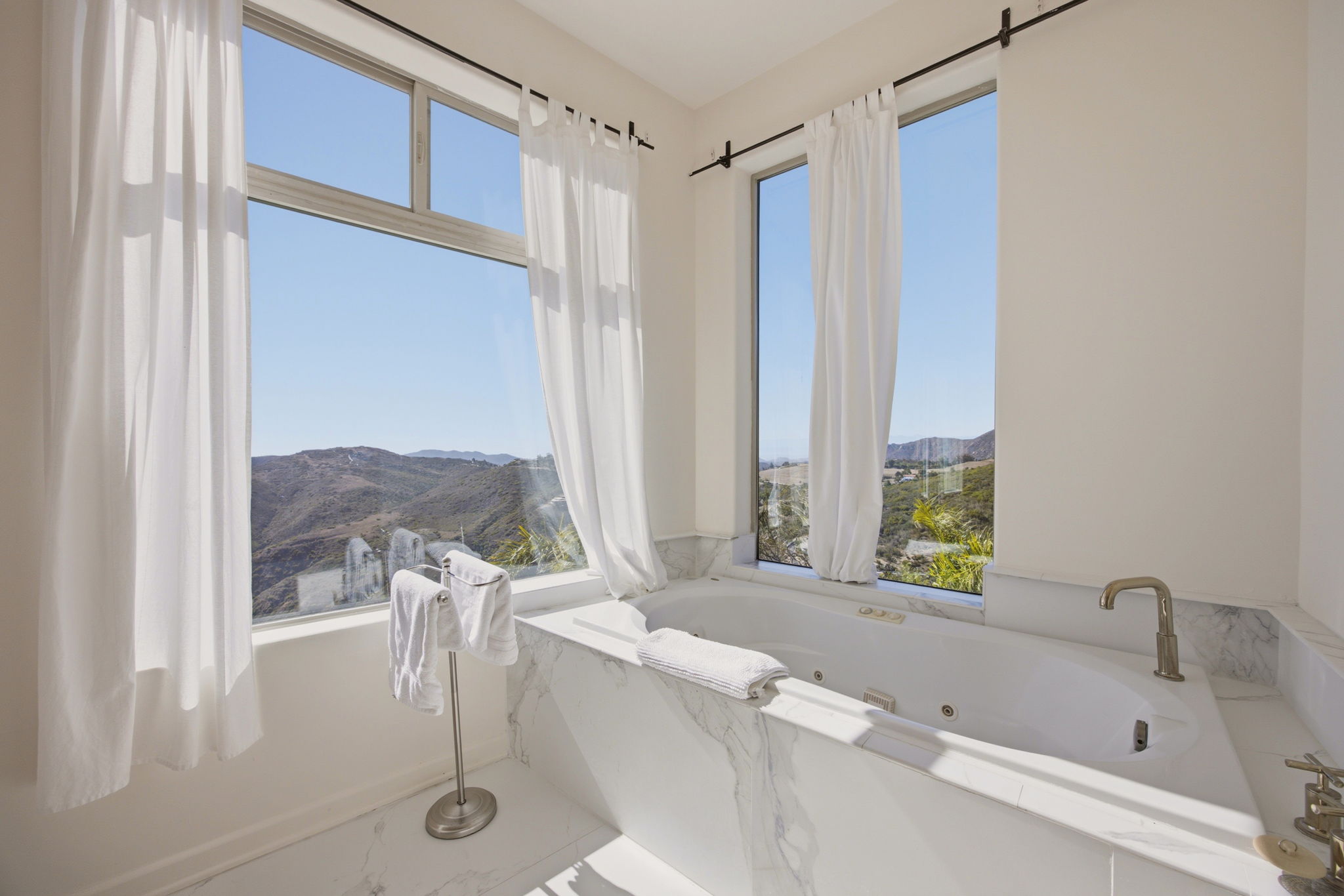 Marble-clad jetted tub set against corner windows with canyon views